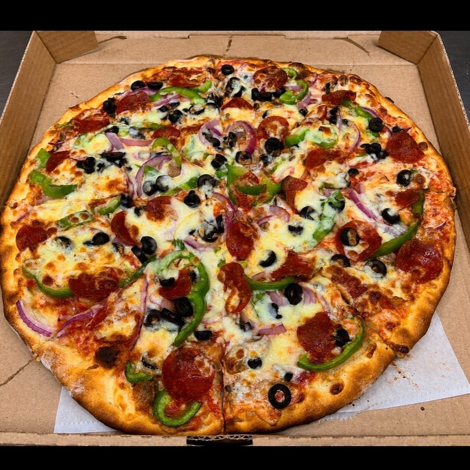 Large loaded pizza topped with pepperoni, green peppers, black olives, red onions, mushrooms, and melted cheese in a cardboard box.