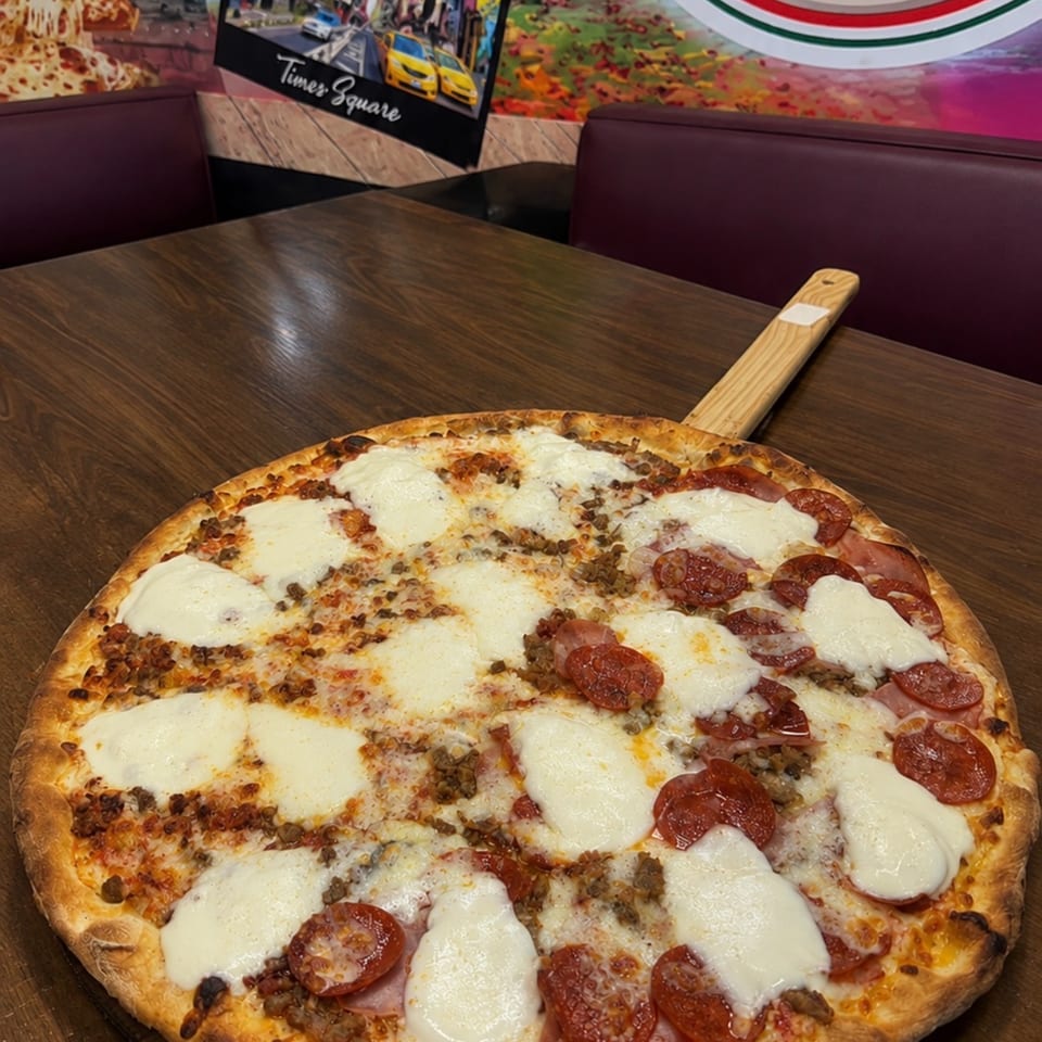 Large pepperoni and mushroom pizza topped with melted cheese on a wooden serving board in a colorful pizzeria booth.